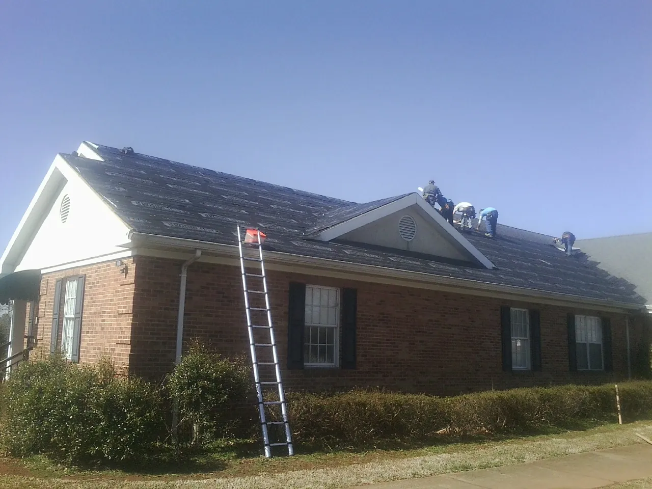 Crew tearing shingles off a brick ranch roof with a ladder set — Emergency Roof Repair work by our crew in Pearl River