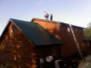 Crew on the ridge of a green metal roof on a two story log home in Pearl River