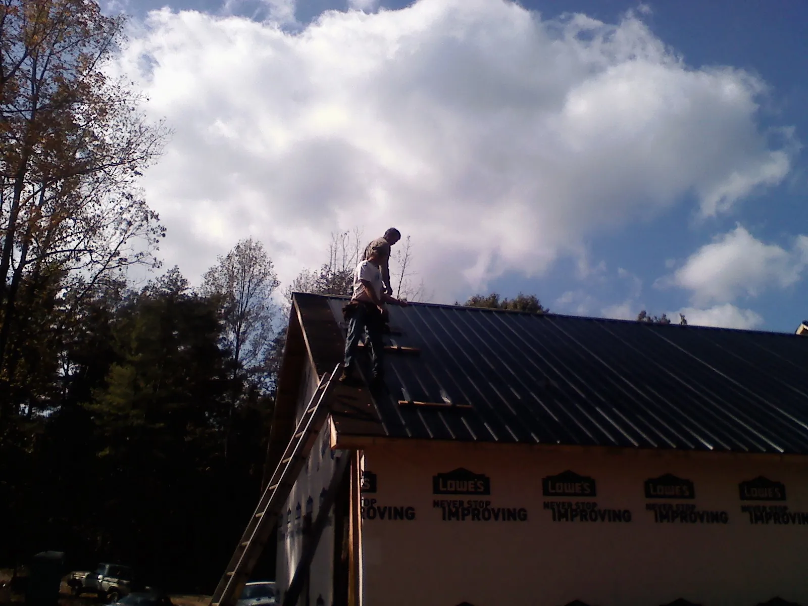 Roofer fastening dark metal panels high against a cloudy sky, from a Roof Inspection job in Pearl River