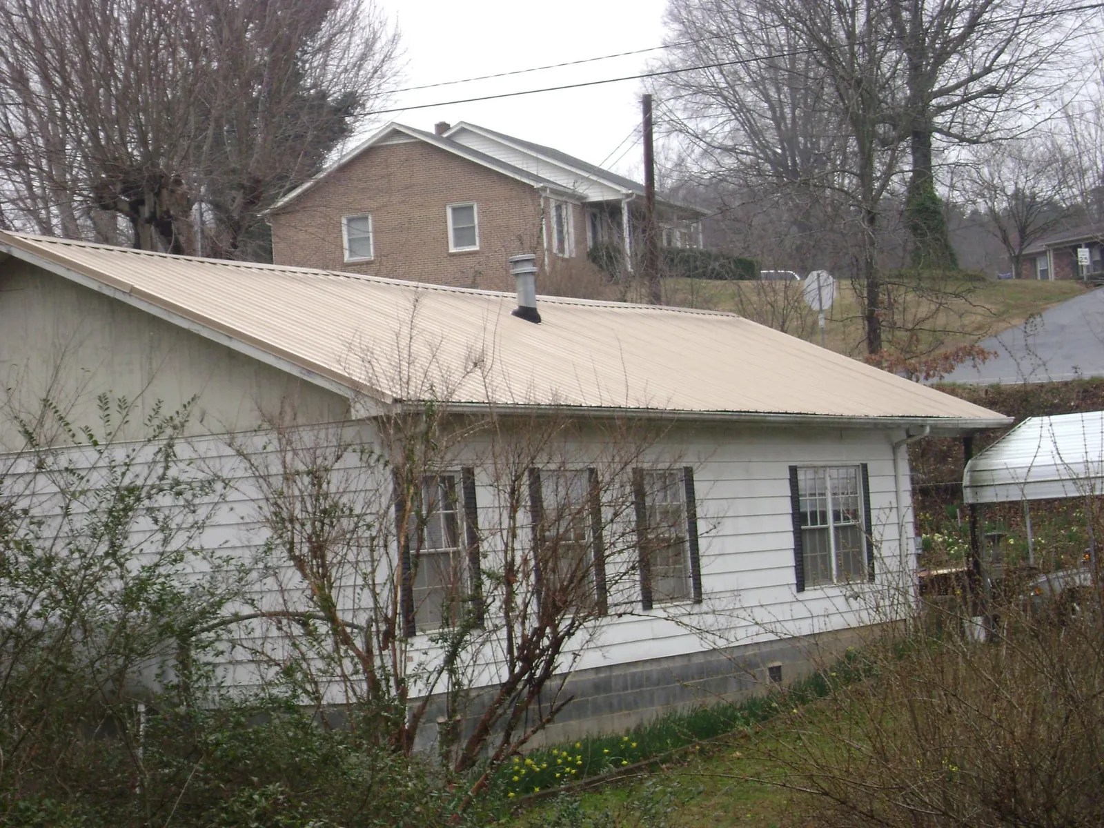 Tan metal roof on a white sided house set into a hillside — Commercial Roofing by Roofing Brothers in Pearl River
