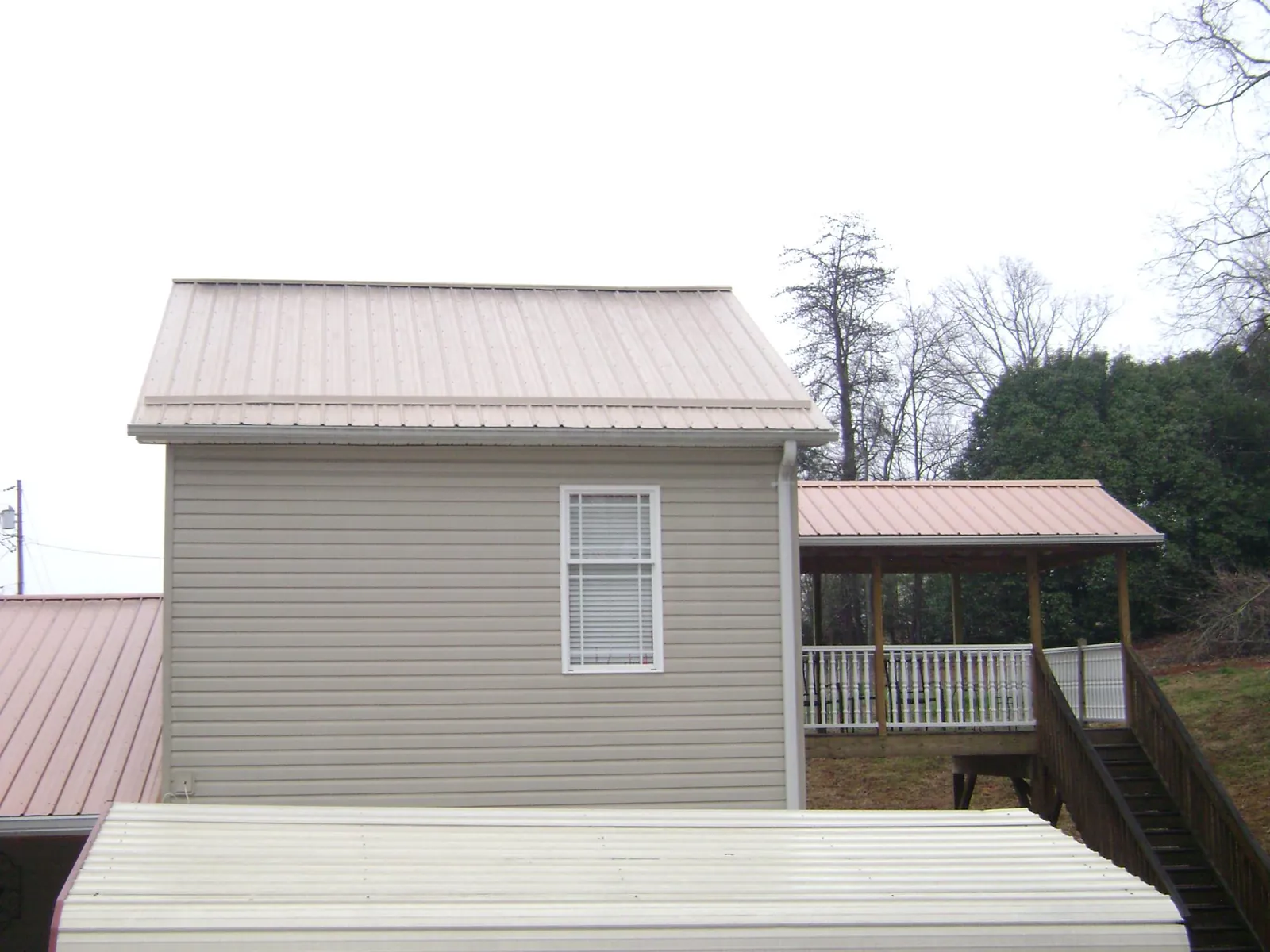 Tan metal roofs on a two story addition and attached porch, from a Roof Replacement job in Pearl River